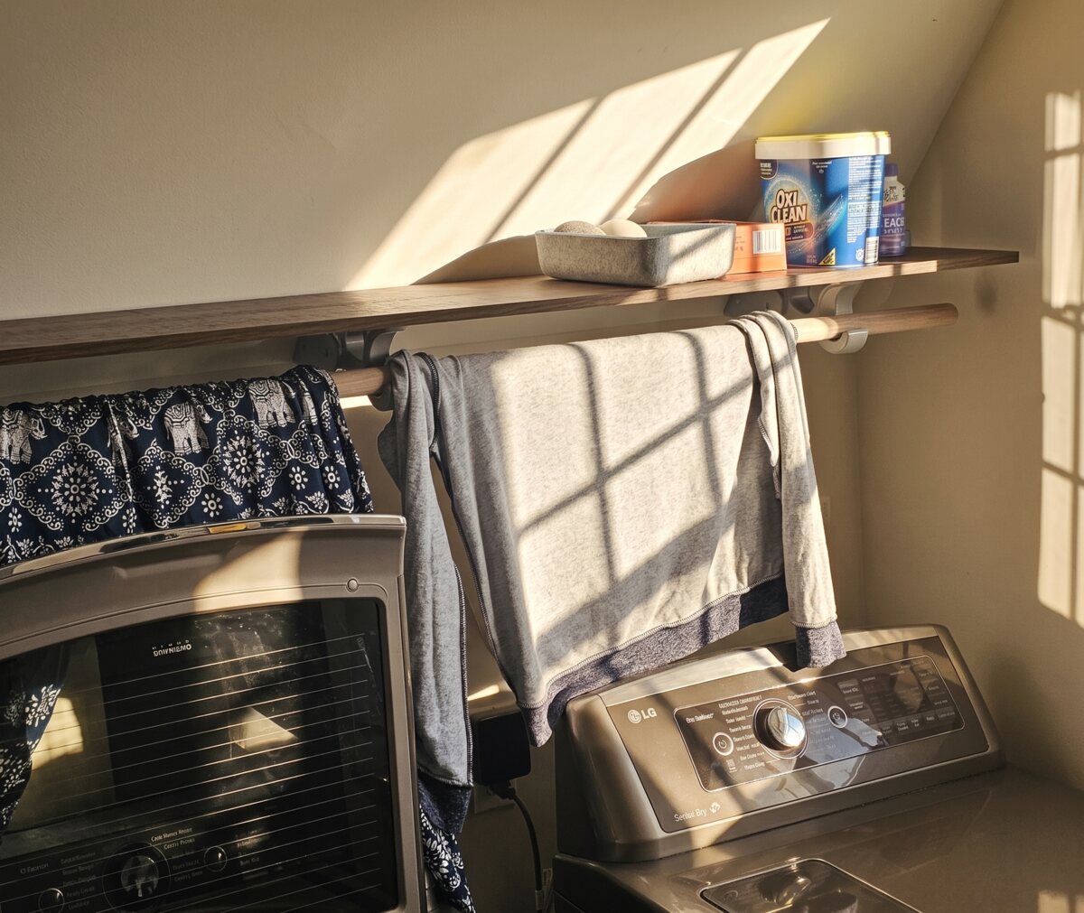 Shelf and hanging rod mounted under the sloped ceiling of a laundry room, a sweatshirt drying on the rod in afternoon light